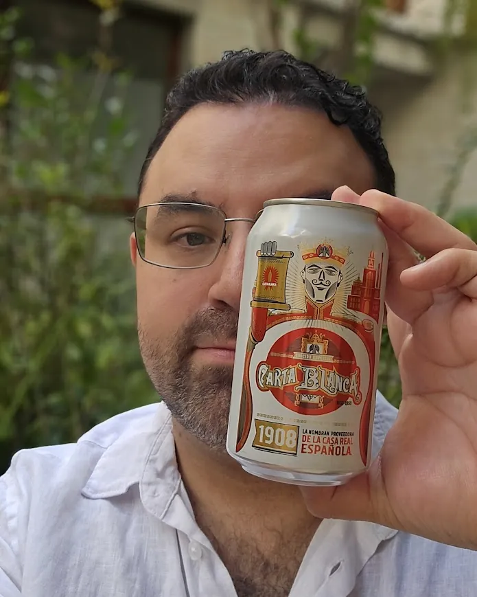 Mario Flores se tapa medio rostro con una lata de Carta Blanca que él ilustró.