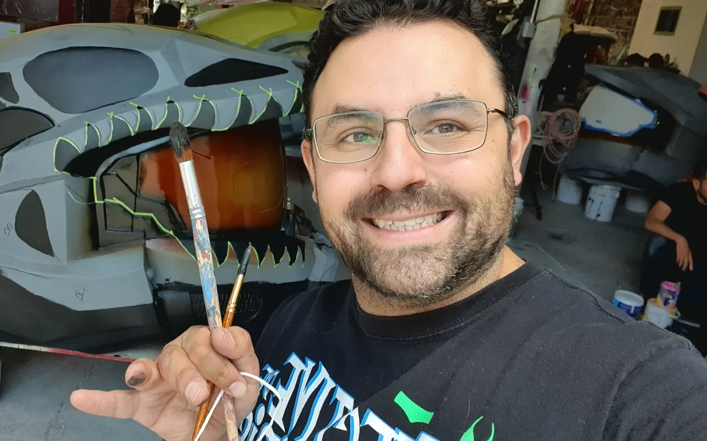 Mario Flores sonríe en una selfie con pinceles en la mano, frente al casco gigante de Master Chief a medio pintar.