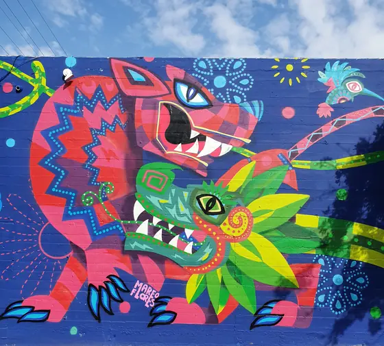 Detalle del mural de Jumex en Los Ángeles: un jaguar rojo y una serpiente emplumada verde sobre una pared azul.