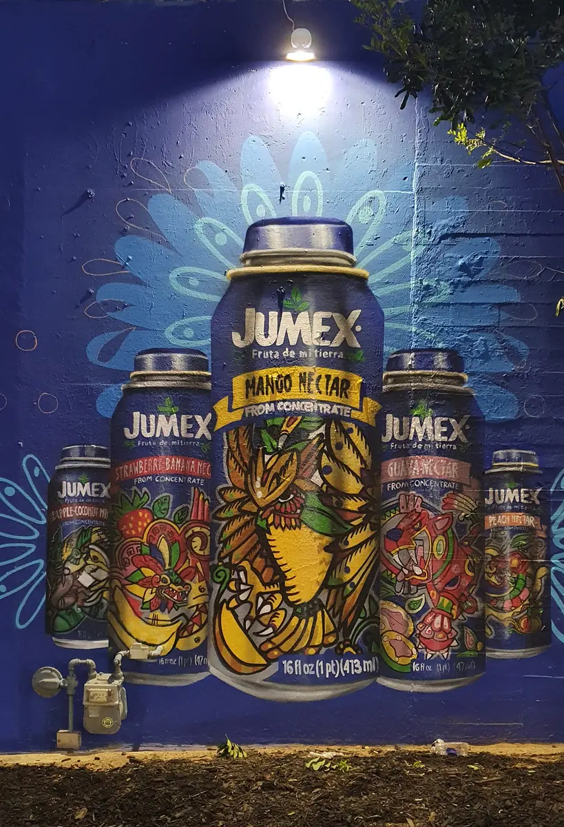 El mural de las latas de Jumex de noche, iluminado por una lámpara.