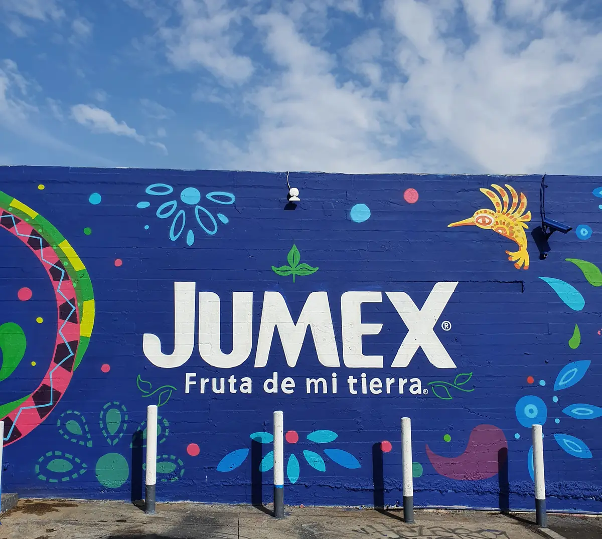 Tramo del mural con el logotipo de Jumex, «Fruta de mi tierra», y un colibrí, bajo el cielo de Los Ángeles.