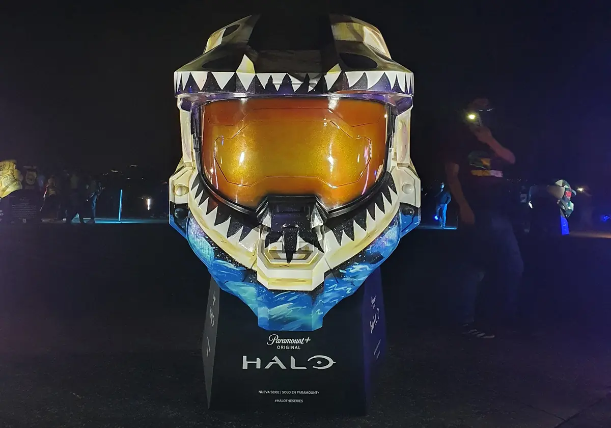 El casco gigante de Master Chief terminado, exhibido de noche sobre su base de Halo: fauces de tiburón con dientes blancos y olas azules.