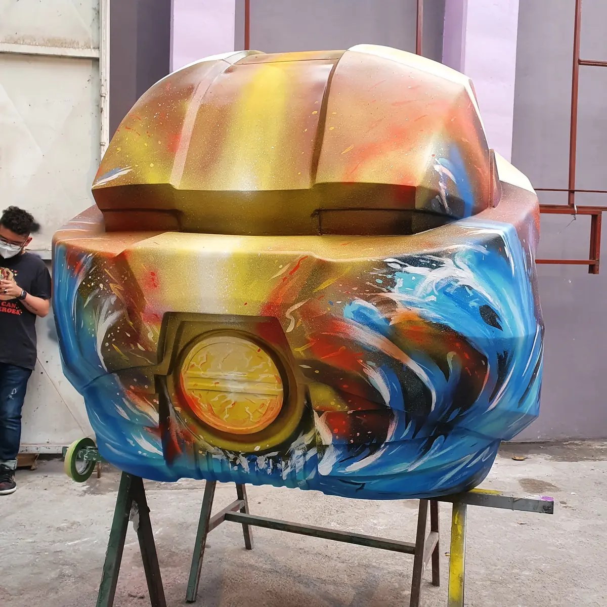 La parte trasera del casco en el taller, pintada con un amanecer dorado sobre olas azules, montada en un caballete.