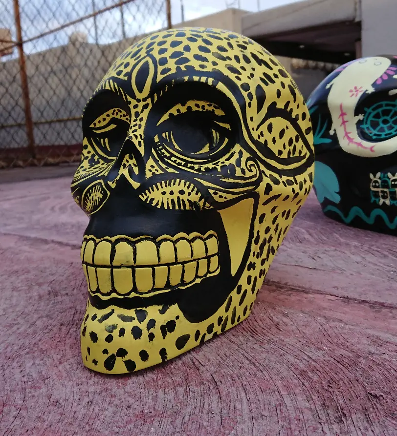 Calavera pintada de amarillo con manchas negras de jaguar y dientes dorados.